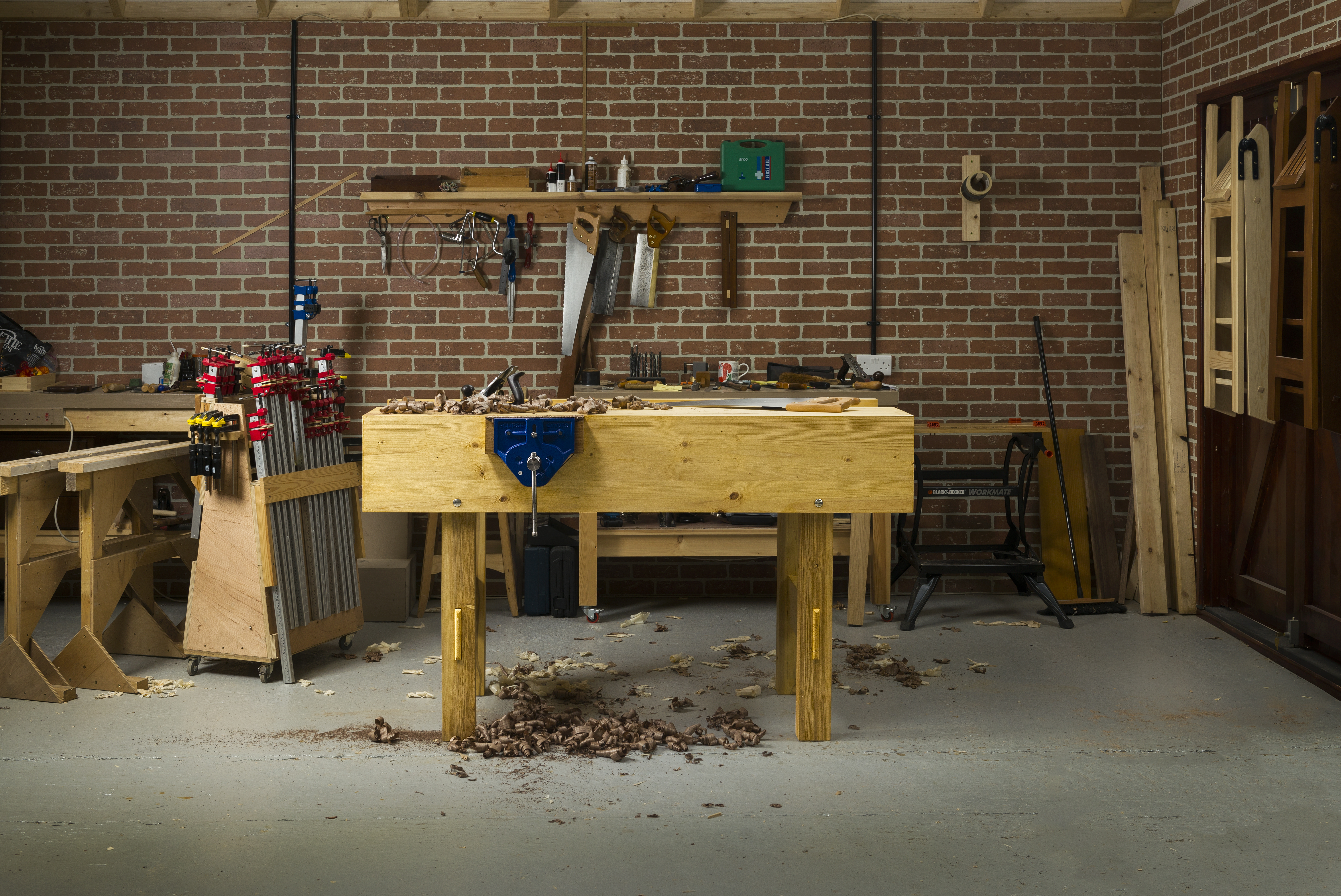 Paul Sellers' workbench in a workshop with brick walls and shavings on the floor. 